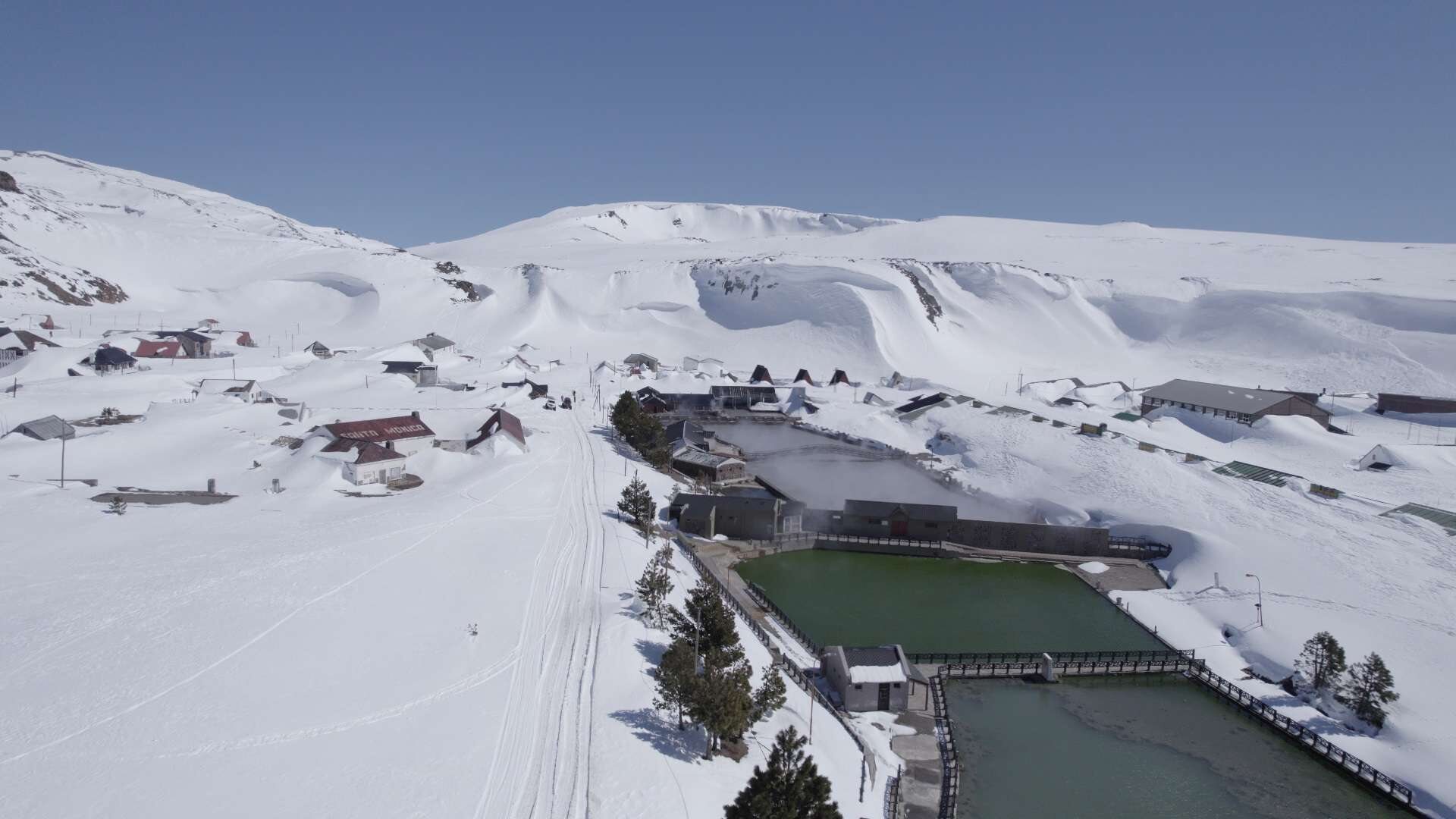 Vista aérea de Copahue bajo la nieve, con las piletas termales y el pueblo al pie de la montaña